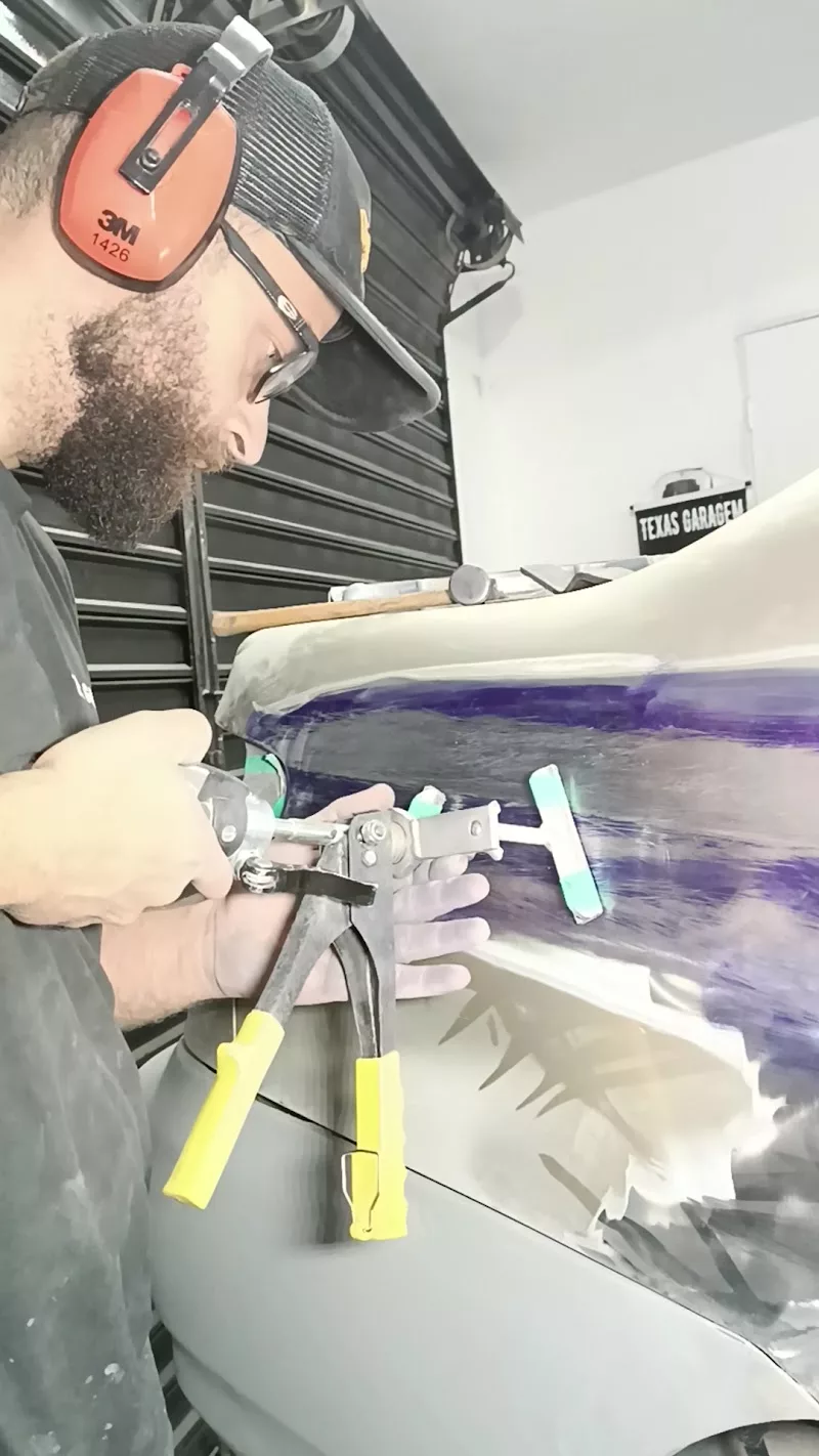 Técnico da Texas Garagem fazendo funilaria manual com martelinho em painel de porta, com o letreiro da marca ao fundo